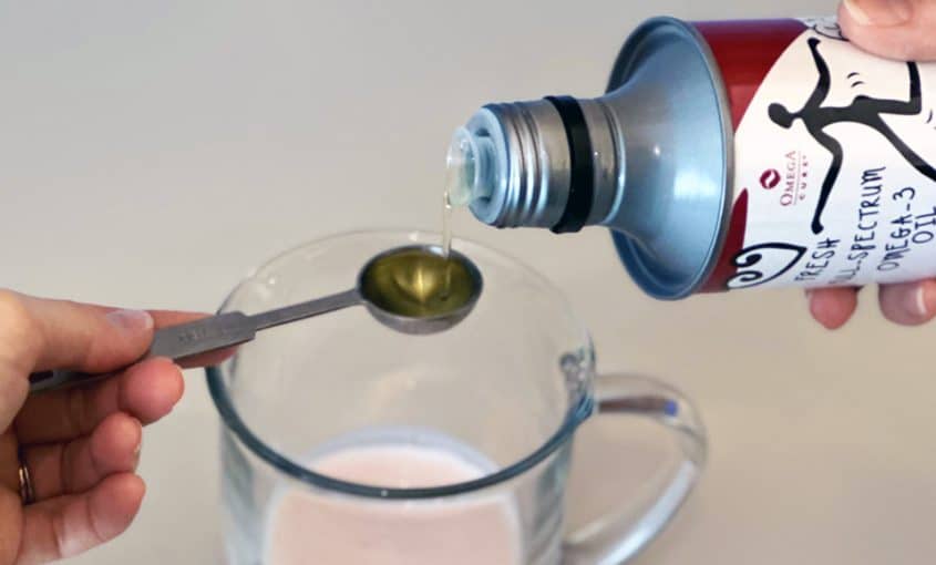 Liquid fish oil being poured onto a measuring spoon