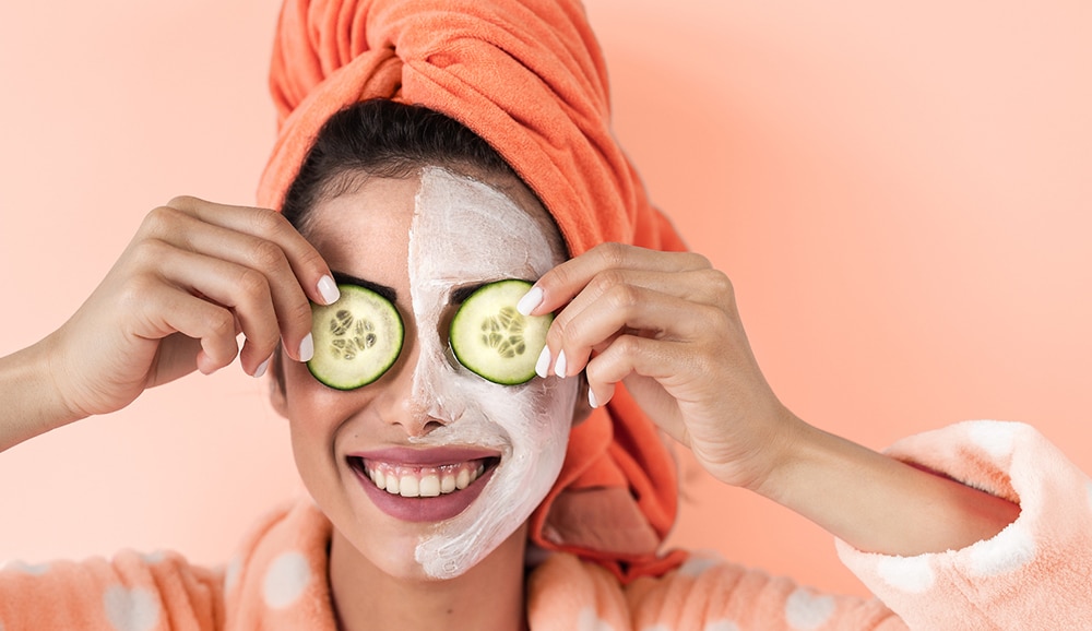 a woman holding cucumber slices over her eyes