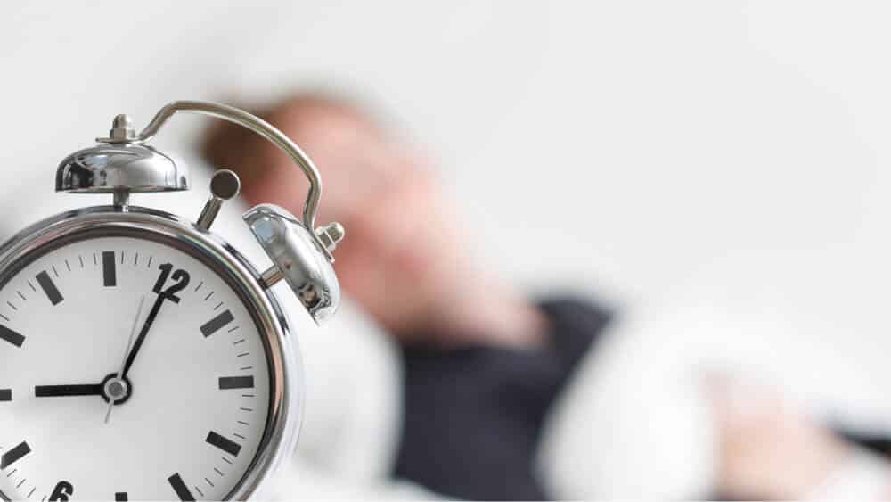 an alarm clock with a person sleeping in the background